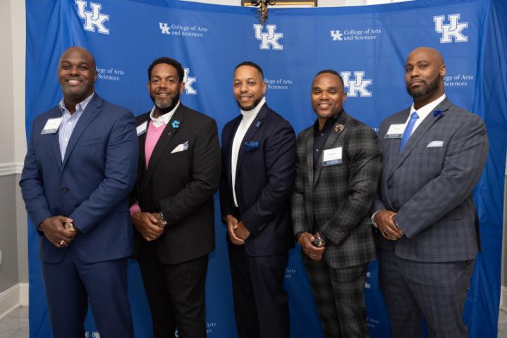 Five attendees pose in front of a backdrop