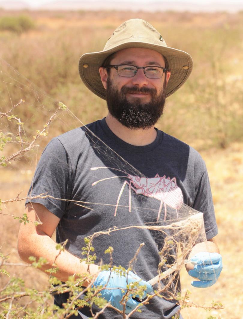 Dr. Nick Keiser out in the fields smiling while holding what looks to be some sort of web.